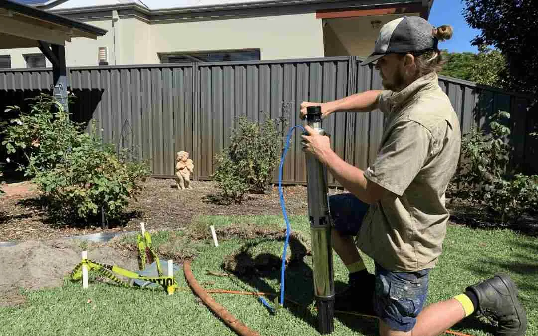 Technician lifting a submersible bore pump from its borehole beside a lawn.
