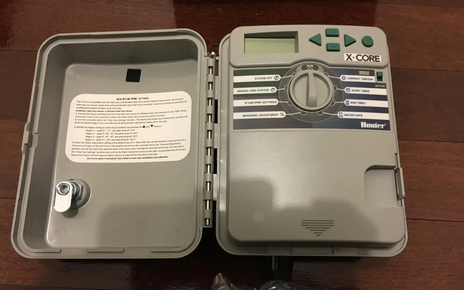 Hunter X-Core outdoor irrigation controller with its weather-resistant cabinet door open, showing the programming dial and LCD display.