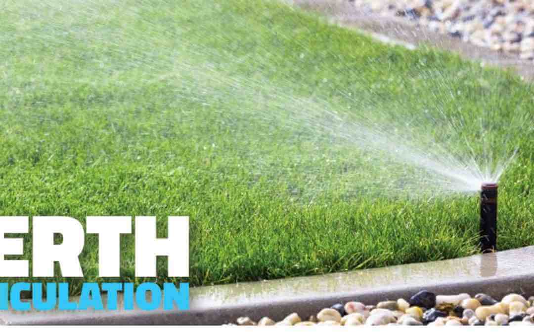 Pop-up sprinkler watering a verge of lush grass with a pebble edge in the foreground.